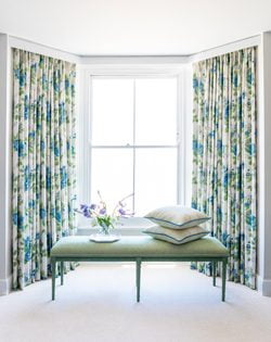 Green bench in front of traditional white-framed sash window, with green and blue curtains in Blithfield either side. White carpet on the floor.